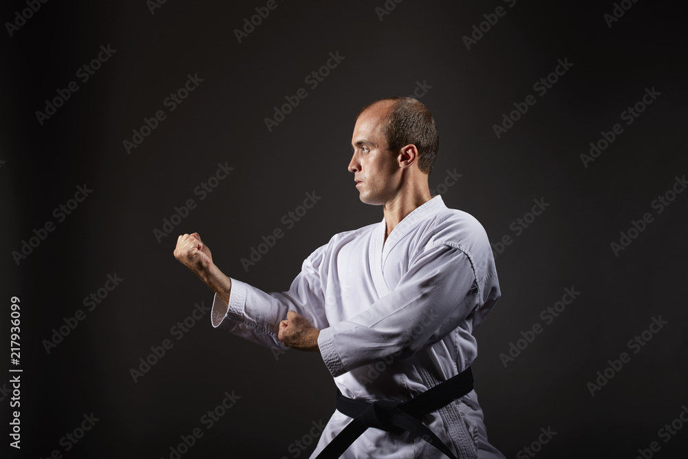 On a black background, an athlete trains a formal karate exercise