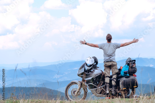 Motorcyclist man stands with his arms outstretched Adventure Motorbike on the top of the mountain. Motorcycle trip. off road Traveling  Lifestyle Travel vacations sport outdoor concept.