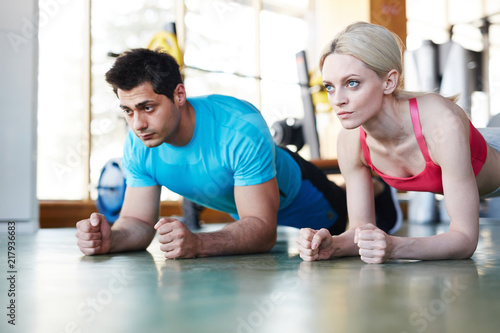 Concentrated woman and woman standing in plank exercise on floor looking forward in gym 
