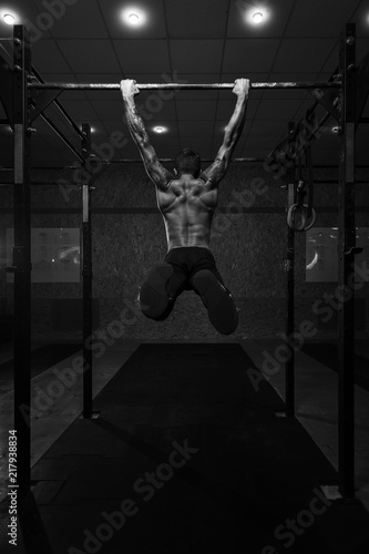 Back view of muscular strong man with naked torso on horizontal bar. fitness, gymnastics workout in gym.