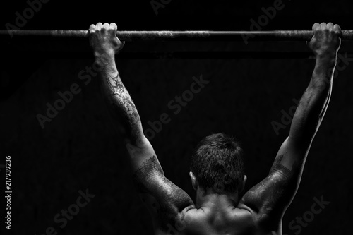 Strong young man doing pull up exercise on horizontal bar in gym. Sports, fitness, gymnastics workout.