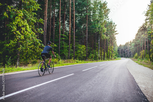 Road bike cyclist, man cycling on empty road in sunset
