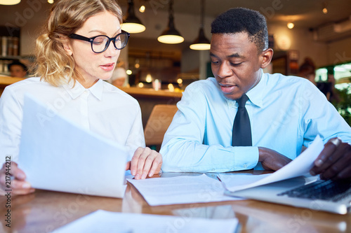 Adult diverse man and woman having meeting and working with papers at table in restaurant