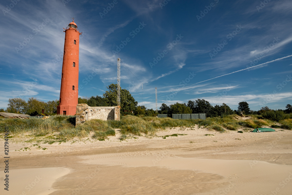 Lighthouse on the coast of the Baltic Sea on a clear blue sky with sand and clouds. Lighthouse Akmenrags, Latvia