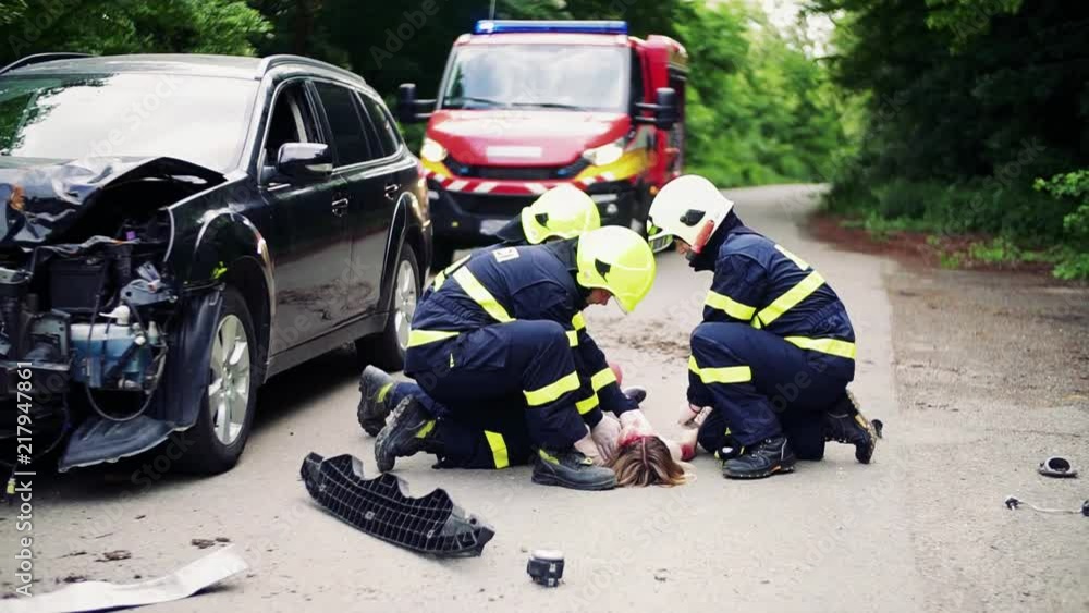 Firefighters rescuing a young injured woman lying on the road after an accident.