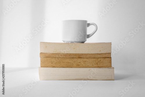 Fototapeta Naklejka Na Ścianę i Meble -  Coffee cup on top of stack of books with white background.