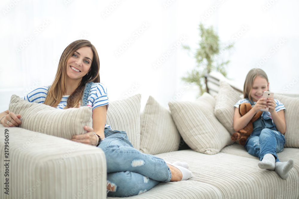 young housewife and her little daughter sitting on the couch young housewife and her little daughter sitting on the couch