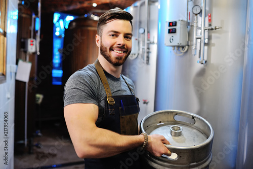 Male brewer with a metal beer barrel on the background of the brewery