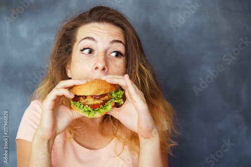 Mindless eating  fast food  unhealthy eating  overeating  self-control  hunger  nutrition concept. Young woman eating greedily big tasty hamburger  copy space