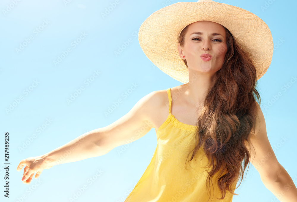 cheerful young woman in straw hat against blue sky