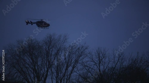 A helicopter depends toward it's landing behind some trees at night. photo