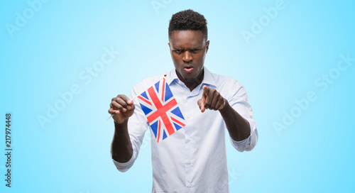 Young african american man holding United Kingdom flag pointing with finger to the camera and to you, hand sign, positive and confident gesture from the front © Krakenimages.com