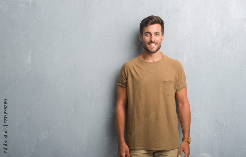 Handsome young man over grey grunge wall with a happy and cool smile on face. Lucky person.