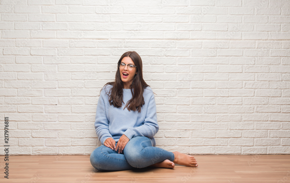Young brunette woman sitting on the floor over white brick wall scared in shock with a surprise face, afraid and excited with fear expression Young brunette woman sitting on the floor over white brick wall scared in shock with a surprise face, afraid and excited with fear expression