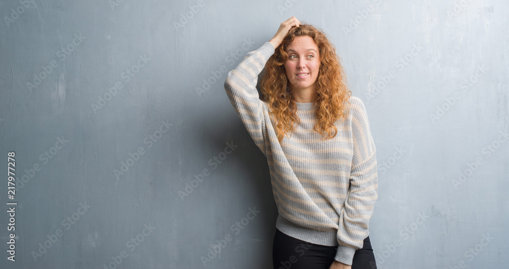 Young redhead woman over grey grunge wall confuse and wonder about question. Uncertain with doubt, thinking with hand on head. Pensive concept. Young redhead woman over grey grunge wall confuse and wonder about question. Uncertain with doubt, thinking with hand on head. Pensive concept.