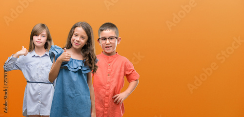Group of boy and girls kids over orange background happy with big smile doing ok sign, thumb up with fingers, excellent sign