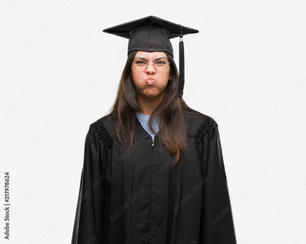 Young hispanic woman wearing graduated cap and uniform puffing cheeks with funny face. Mouth inflated with air, crazy expression. Young hispanic woman wearing graduated cap and uniform puffing cheeks with funny face. Mouth inflated with air, crazy expression.