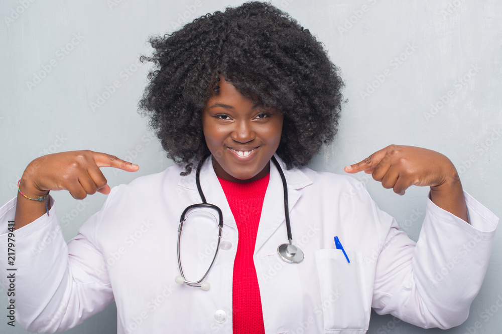 Young african american doctor woman over grey grunge wall looking confident with smile on face, pointing oneself with fingers proud and happy. Young african american doctor woman over grey grunge wall looking confident with smile on face, pointing oneself with fingers proud and happy.