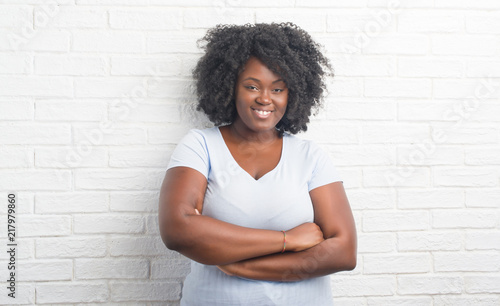 Young african american plus size woman over white brick wall happy face smiling with crossed arms looking at the camera. Positive person.