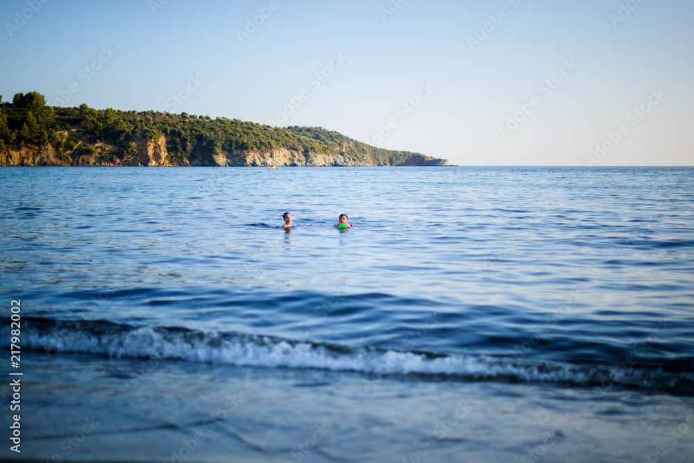 Two kids swiming into the blue sea