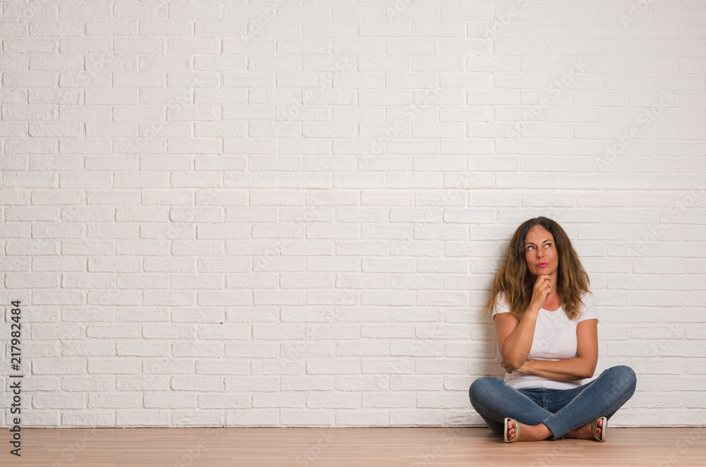 Middle age hispanic woman over white brick wall serious face thinking about question, very confused idea Middle age hispanic woman over white brick wall serious face thinking about question, very confused idea