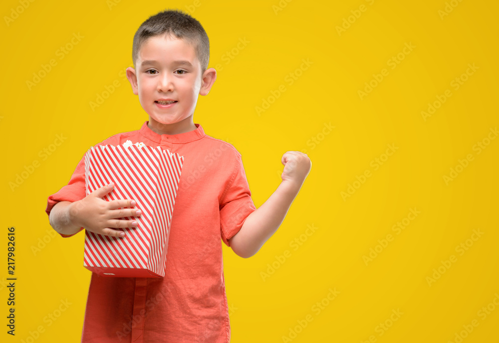 Dark haired little child eating popcorn screaming proud and celebrating victory and success very excited, cheering emotion Dark haired little child eating popcorn screaming proud and celebrating victory and success very excited, cheering emotion