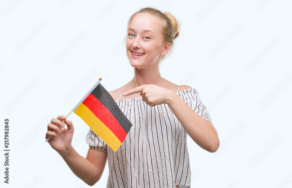 Blonde teenager woman holding flag of Germany very happy pointing with hand and finger Blonde teenager woman holding flag of Germany very happy pointing with hand and finger