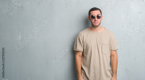 Young caucasian man over grey grunge wall wearing sunglasses depressed and worry for distress, crying angry and afraid. Sad expression. © Krakenimages.com