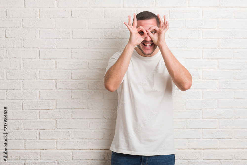 Young caucasian man standing over white brick wall confuse and wonder about question. Uncertain with doubt, thinking with hand on head. Pensive concept. Young caucasian man standing over white brick wall confuse and wonder about question. Uncertain with doubt, thinking with hand on head. Pensive concept.