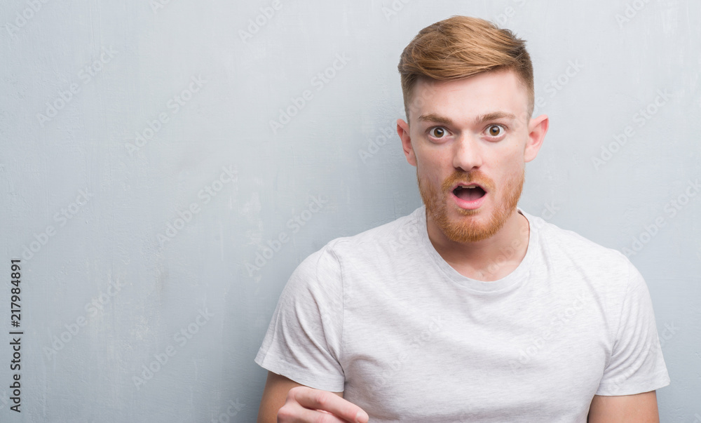Obraz premium Young redhead man over grey grunge wall scared in shock with a surprise face, afraid and excited with fear expression