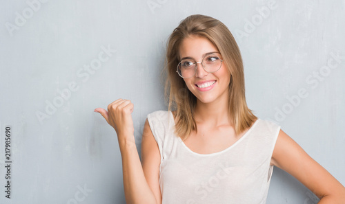 Wallpaper Mural Beautiful young woman standing over grunge grey wall wearing glasses pointing and showing with thumb up to the side with happy face smiling Torontodigital.ca