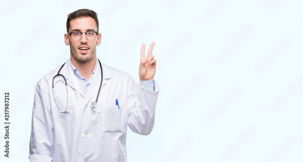 Handsome young doctor man smiling with happy face winking at the camera doing victory sign. Number two. Handsome young doctor man smiling with happy face winking at the camera doing victory sign. Number two.