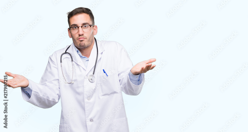 Handsome young doctor man clueless and confused expression with arms and hands raised. Doubt concept. Handsome young doctor man clueless and confused expression with arms and hands raised. Doubt concept.