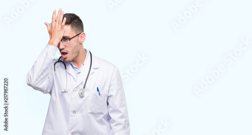 Handsome young doctor man surprised with hand on head for mistake, remember error. Forgot, bad memory concept. © Krakenimages.com