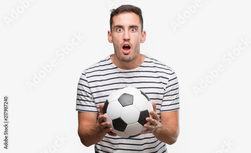 Handsome young man holding soccer football scared in shock with a surprise face, afraid and excited with fear expression