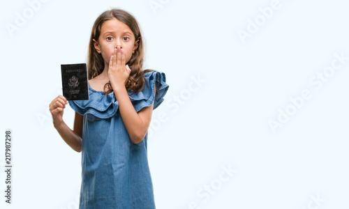 Brunette hispanic girl holding passport of United States of America cover mouth with hand shocked with shame for mistake, expression of fear, scared in silence, secret concept