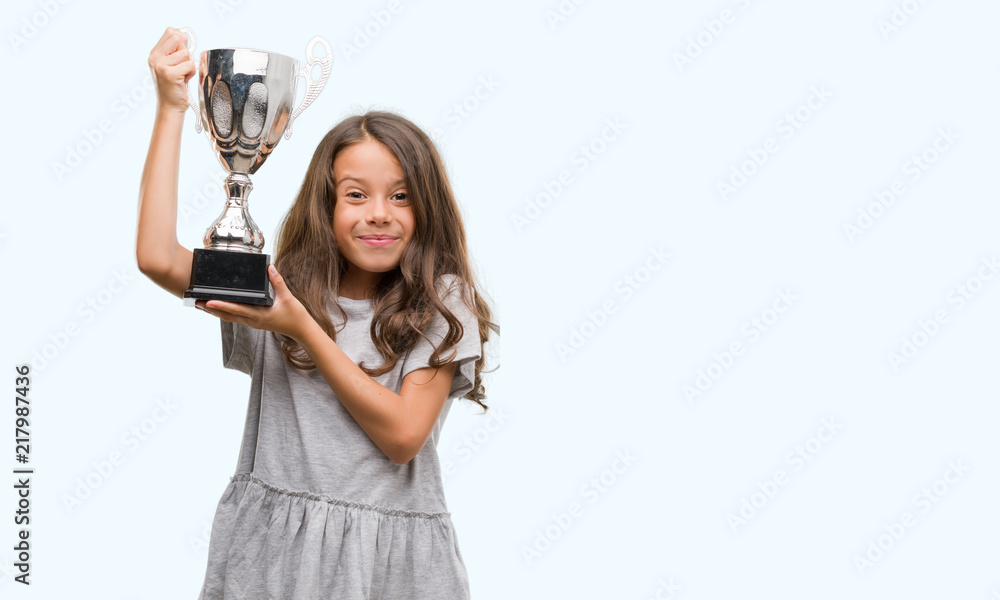 Brunette hispanic girl holding a trophy with a happy face standing and smiling with a confident smile showing teeth Brunette hispanic girl holding a trophy with a happy face standing and smiling with a confident smile showing teeth