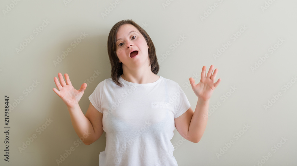 Down syndrome woman standing over wall crazy and mad shouting and yelling with aggressive expression and arms raised. Frustration concept. Down syndrome woman standing over wall crazy and mad shouting and yelling with aggressive expression and arms raised. Frustration concept.