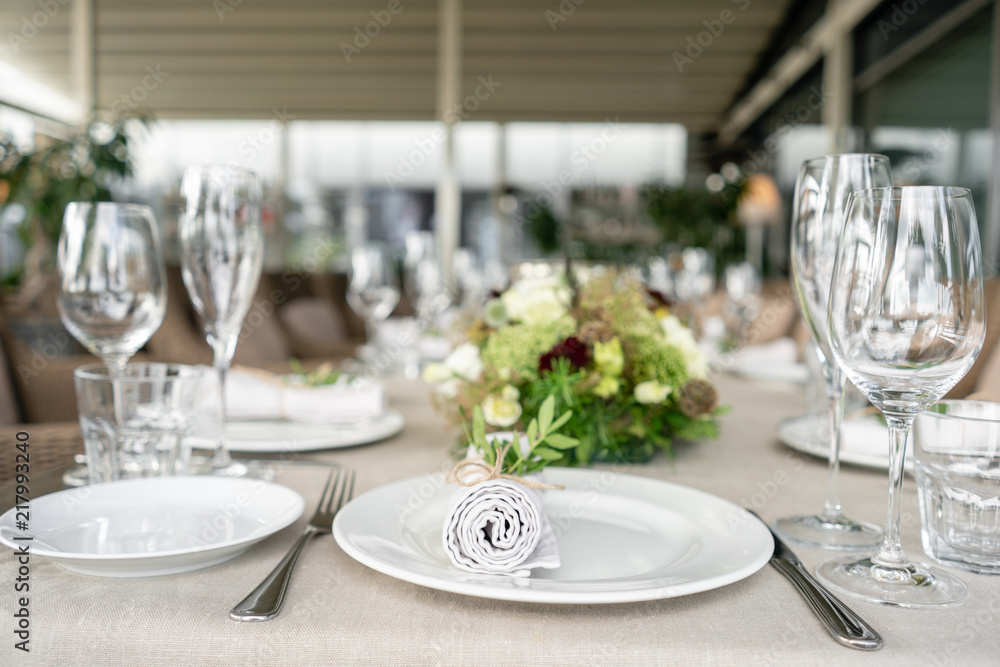 Neatly twisted into a tube dining room napkin decorated with a sprig of pistachio. Wedding Banquet or gala dinner. The chairs and table for guests, served with cutlery and crockery. party on terrace