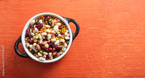 Assortment of legumes pulses in enameled bowl on orange background, isolated, top view, copy space.