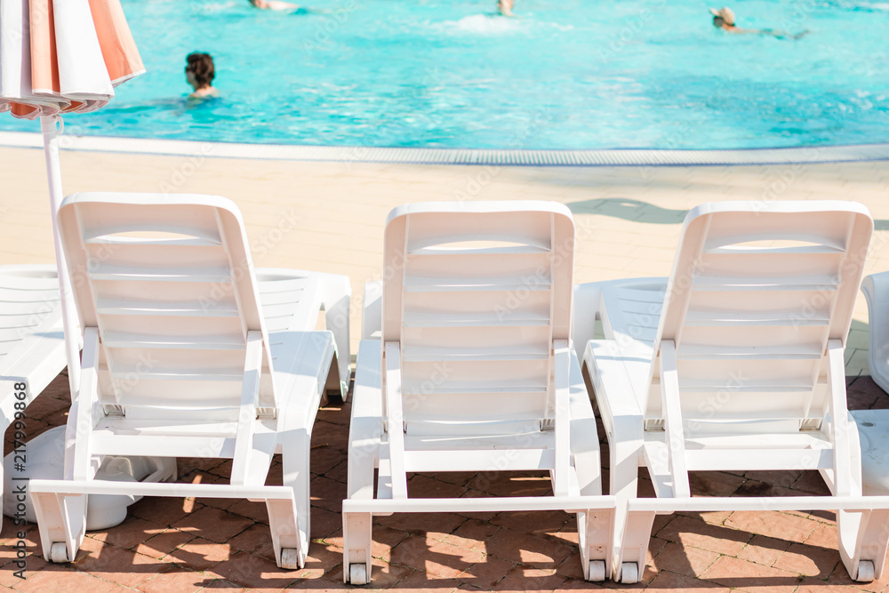Fototapeta premium White loungers near the swimming pool on a summer day.
