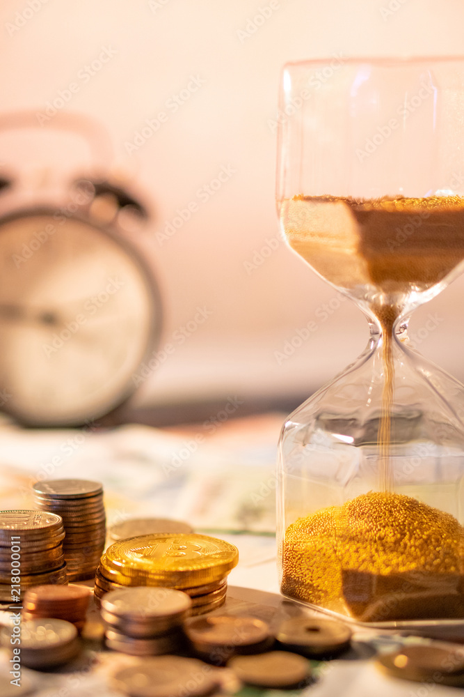 Sand running through the shape of hourglass on table with banknotes and coins of international currency. Time investment and retirement saving. Urgency countdown timer for business deadline concept Sand running through the shape of hourglass on table with banknotes and coins of international currency. Time investment and retirement saving. Urgency countdown timer for business deadline concept