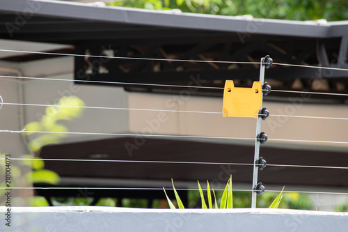 high voltage security fence on house wall with blank yellow plastice sign. photo