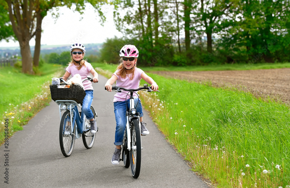 Fototapeta premium Twin sisters ride their bicycles with scenic landscape around them. They have happy smiling faces on them as they enjoy the outdoor cycle tour.