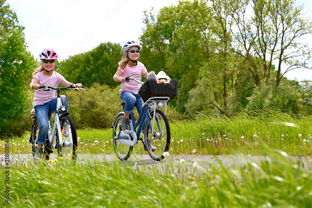 Twin sisters ride their bicycles with scenic landscape around them. They have happy smiling faces on them as they enjoy the outdoor cycle tour. Twin sisters ride their bicycles with scenic landscape around them. They have happy smiling faces on them as they enjoy the outdoor cycle tour.