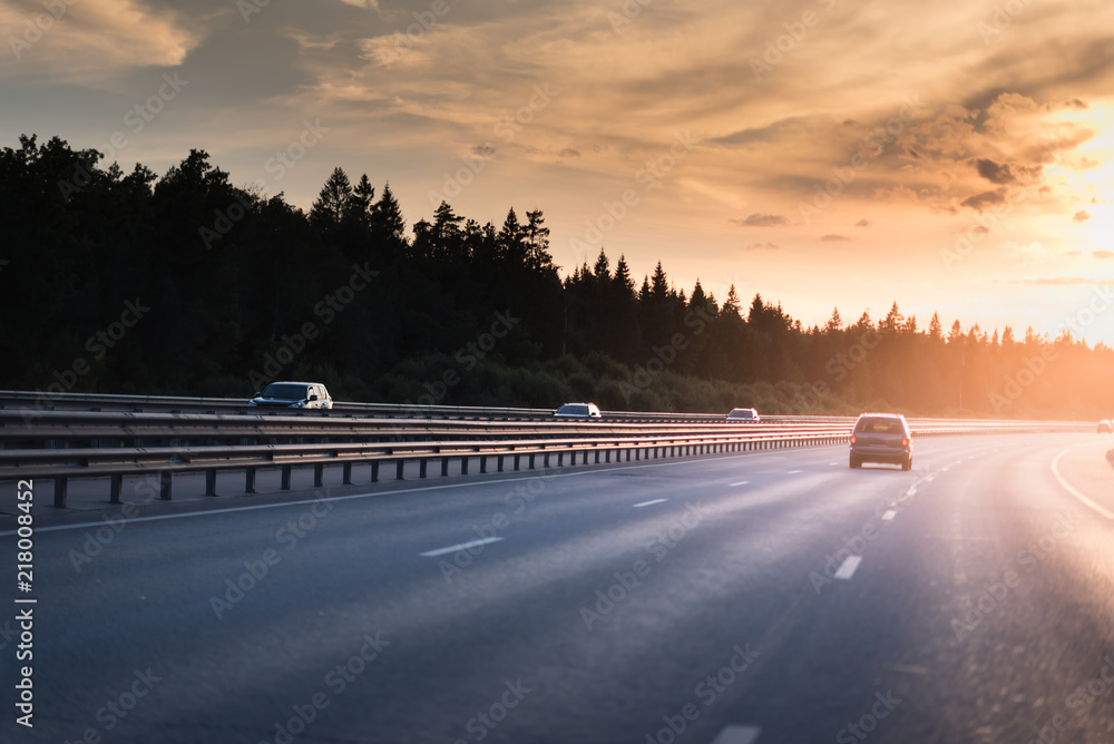 Fototapeta premium Highway traffic in sunset. minivan on the asphalt road with metal safety barrier or rail. Pine forest on the background