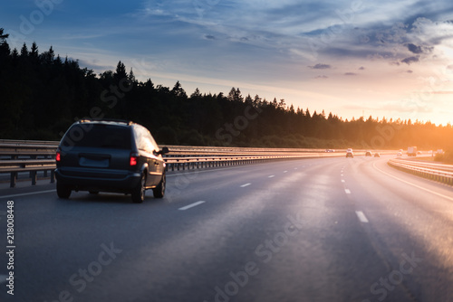 Highway traffic in sunset. minivan on the asphalt road with metal safety barrier or rail. Pine forest on the background © Mak