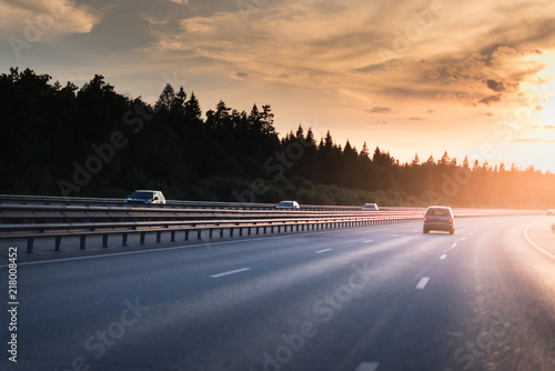 Highway traffic in sunset. minivan on the asphalt road with metal safety barrier or rail. Pine forest on the background
