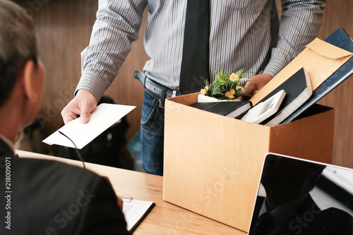 Business man sending resignation letter to boss and Holding Stuff Resign Depress or carrying cardboard box by desk in office.