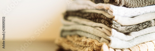 Stack of cozy knitted clothes on a wooden stand. banner, long wide